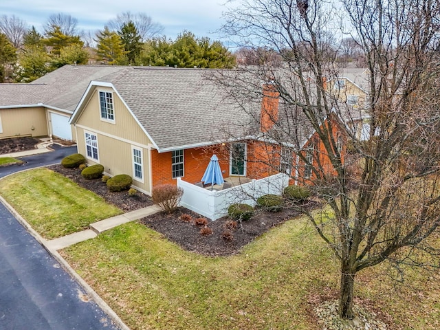 view of front of home featuring a garage, a shingled roof, brick siding, driveway, and a front yard