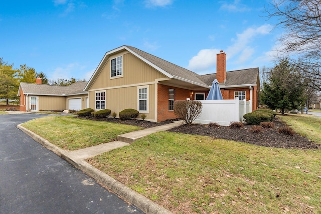 view of front of property featuring an attached garage, brick siding, fence, driveway, and a chimney