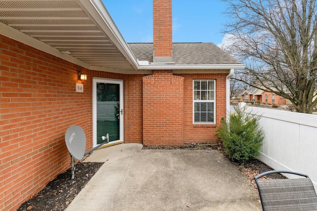 exterior space featuring brick siding, a patio, a chimney, a shingled roof, and fence