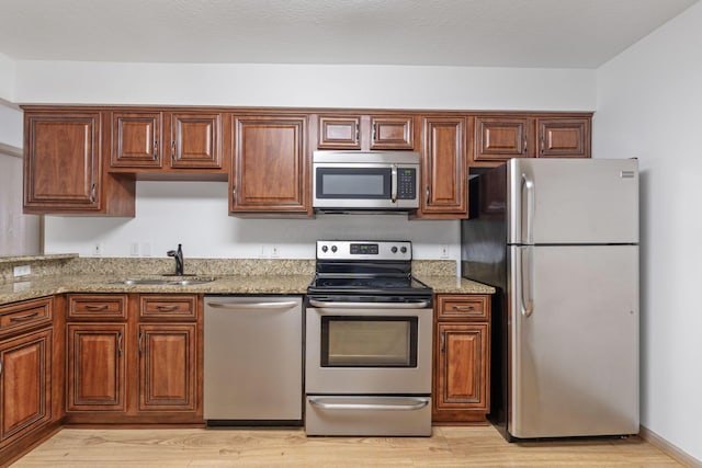 kitchen with light stone counters, appliances with stainless steel finishes, sink, and light hardwood / wood-style flooring