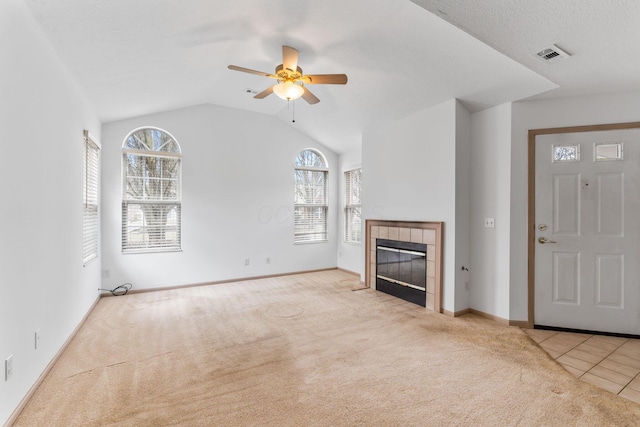 unfurnished living room with vaulted ceiling, light carpet, a textured ceiling, ceiling fan, and a tiled fireplace