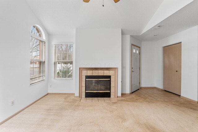 unfurnished living room with light carpet, a tiled fireplace, vaulted ceiling, and ceiling fan