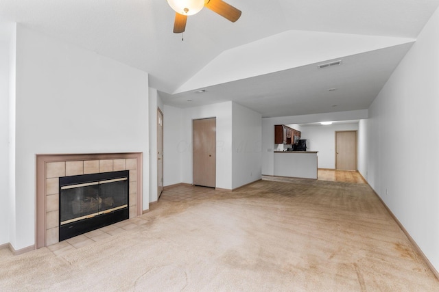 unfurnished living room featuring a tiled fireplace, vaulted ceiling, light carpet, and ceiling fan