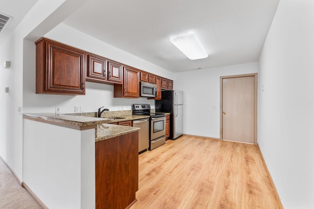 kitchen with sink, a textured ceiling, stainless steel appliances, light stone countertops, and light hardwood / wood-style floors