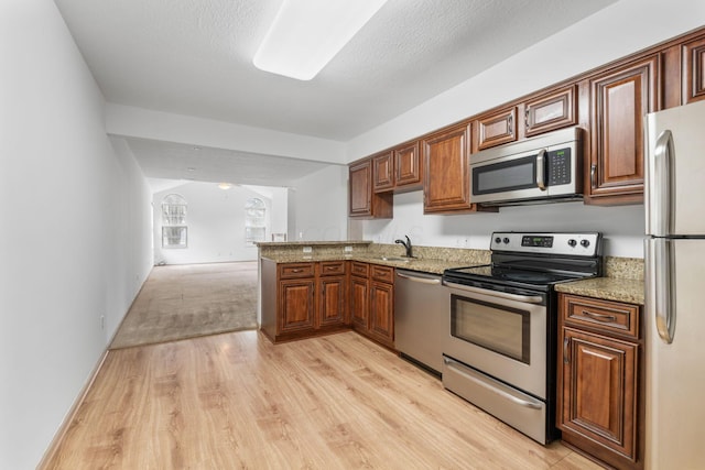 kitchen featuring appliances with stainless steel finishes, sink, kitchen peninsula, light stone countertops, and light wood-type flooring