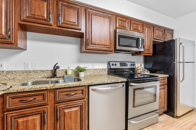 kitchen with stainless steel appliances, brown cabinets, a sink, and light stone counters