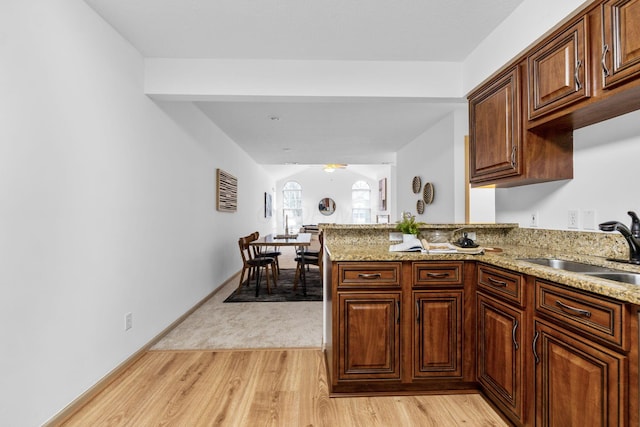 kitchen with a peninsula, light stone counters, a sink, and light wood-style floors