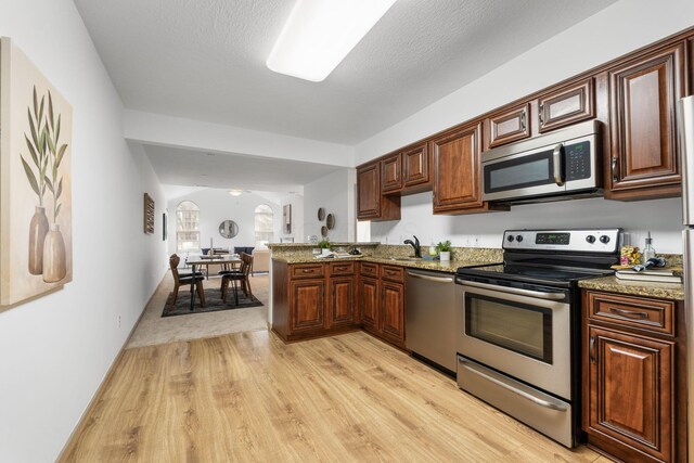 kitchen with light stone counters, stainless steel appliances, a peninsula, a sink, and light wood-type flooring