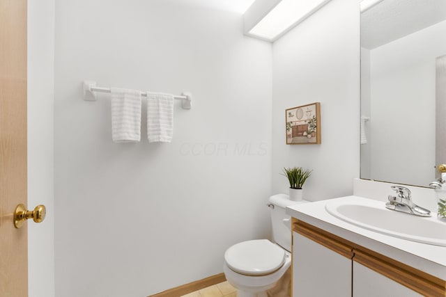 half bathroom featuring a skylight, tile patterned flooring, vanity, and toilet