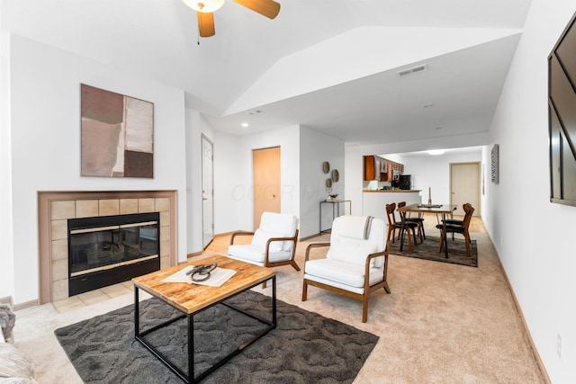 living room featuring light carpet, visible vents, vaulted ceiling, and a tiled fireplace