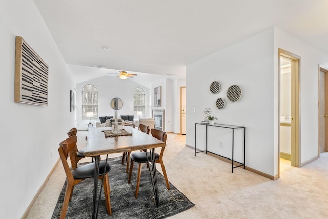 dining room with baseboards, a ceiling fan, a glass covered fireplace, lofted ceiling, and light colored carpet