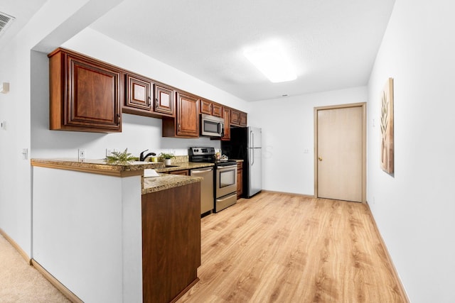 kitchen with a peninsula, baseboards, appliances with stainless steel finishes, light stone countertops, and light wood finished floors