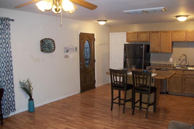 kitchen with a breakfast bar, black refrigerator, hardwood / wood-style floors, ceiling fan, and sink