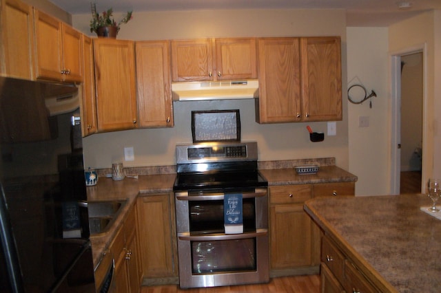 kitchen featuring sink, black refrigerator, light wood-type flooring, and range with two ovens