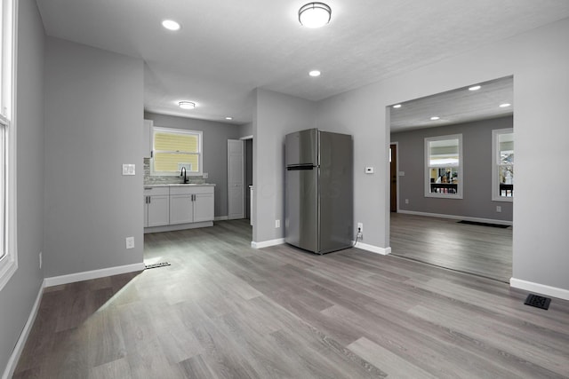 kitchen with sink, white cabinets, stainless steel refrigerator, and light wood-type flooring