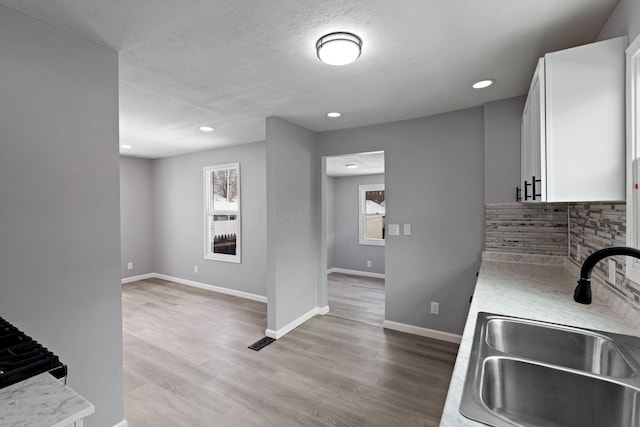 kitchen featuring sink, white cabinets, a textured ceiling, light hardwood / wood-style floors, and decorative backsplash