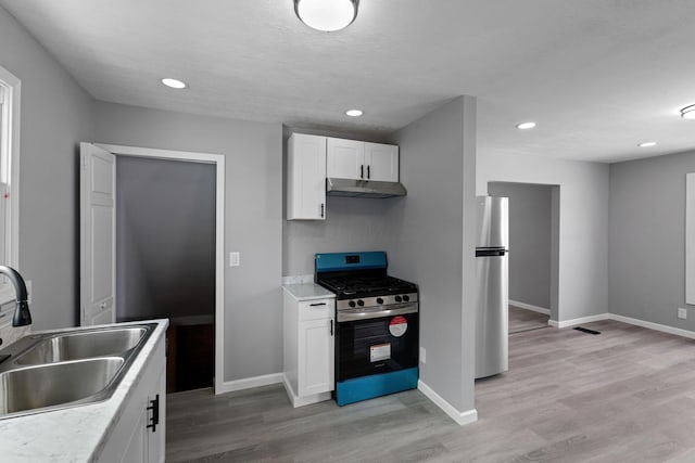 kitchen with a textured ceiling, stainless steel appliances, light wood-type flooring, white cabinetry, and sink