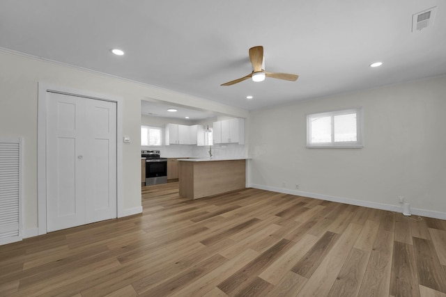 kitchen with light hardwood / wood-style floors, kitchen peninsula, decorative backsplash, white cabinetry, and stainless steel electric range oven