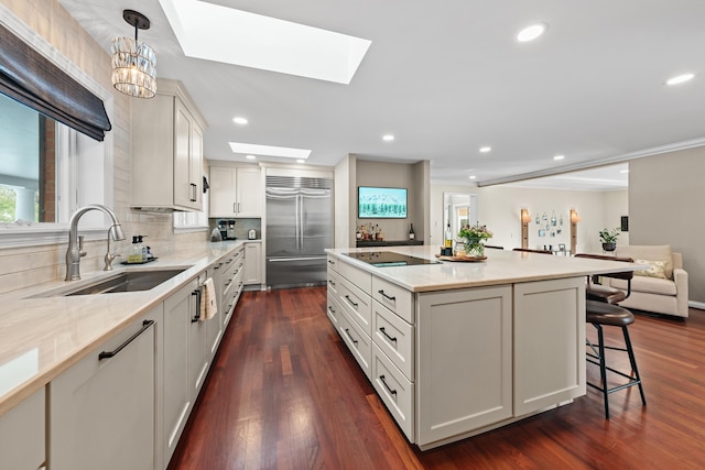 kitchen with a skylight, stainless steel built in fridge, a center island, pendant lighting, and sink