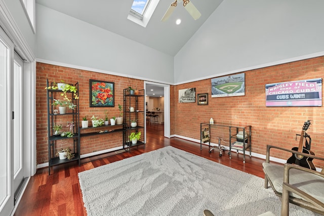 interior space with a skylight, ceiling fan, dark hardwood / wood-style floors, brick wall, and high vaulted ceiling