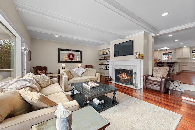 living room with crown molding, a fireplace, hardwood / wood-style flooring, and beamed ceiling