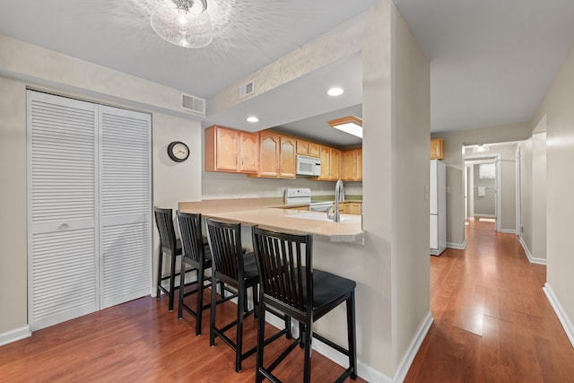 kitchen with hardwood / wood-style flooring, kitchen peninsula, a breakfast bar area, white appliances, and light brown cabinetry