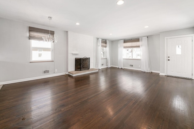 unfurnished living room featuring a brick fireplace, dark wood-type flooring, and a healthy amount of sunlight