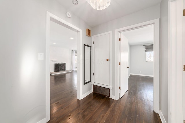 corridor with dark wood-type flooring and an inviting chandelier