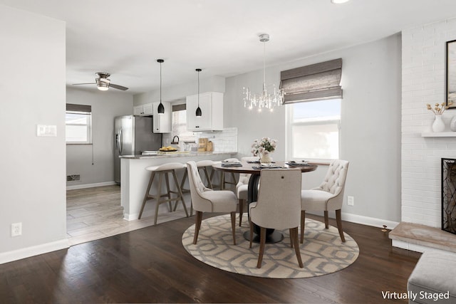 dining room featuring ceiling fan with notable chandelier, hardwood / wood-style floors, and a fireplace