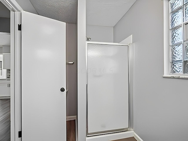 bathroom featuring a wealth of natural light, an enclosed shower, a textured ceiling, and hardwood / wood-style floors