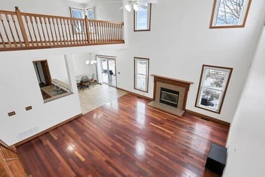 unfurnished living room with baseboards, ceiling fan, a towering ceiling, wood finished floors, and a glass covered fireplace