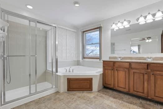 full bathroom with a ceiling fan, a sink, a shower stall, double vanity, and a bath