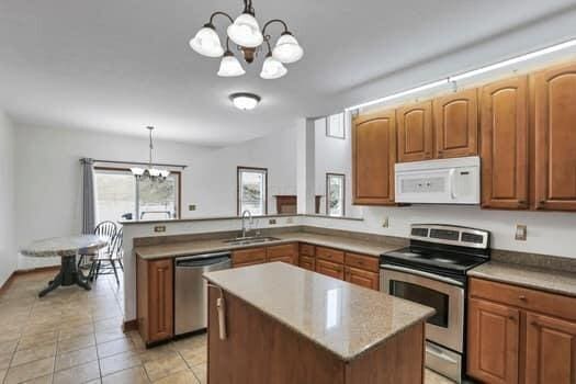 kitchen featuring a peninsula, plenty of natural light, a sink, stainless steel appliances, and a chandelier