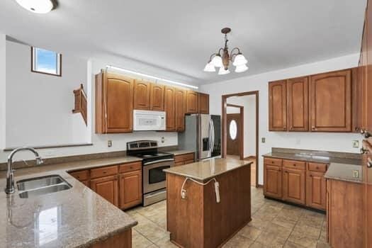 kitchen with a center island, brown cabinets, hanging light fixtures, stainless steel appliances, and a sink