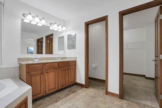 full bath featuring double vanity, a bath, baseboards, and a sink