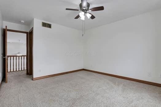 carpeted spare room with visible vents, baseboards, and ceiling fan