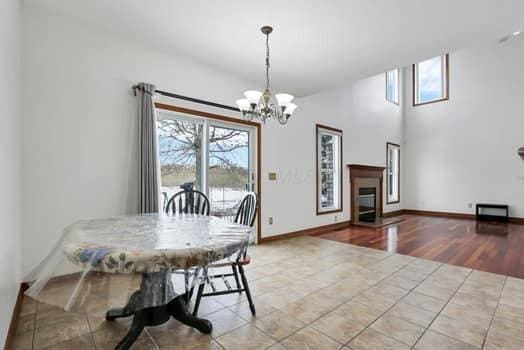 tiled dining room with a glass covered fireplace, baseboards, and an inviting chandelier