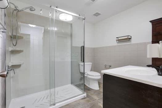 bathroom featuring toilet, a stall shower, tile walls, wainscoting, and vanity