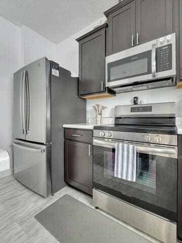 kitchen featuring a textured ceiling, dark brown cabinetry, stainless steel appliances, baseboards, and light countertops