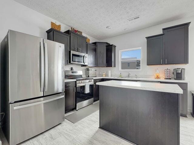 kitchen with visible vents, a center island, stainless steel appliances, light countertops, and a sink