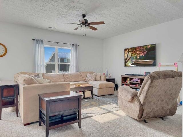 living room with light carpet, ceiling fan, and a textured ceiling