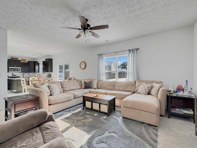 living room with ceiling fan, a textured ceiling, and light colored carpet