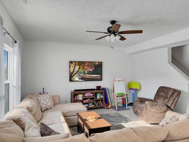 living area featuring carpet, a ceiling fan, and a textured ceiling