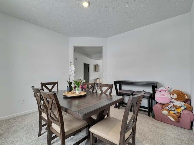 dining area featuring baseboards, a textured ceiling, and light colored carpet