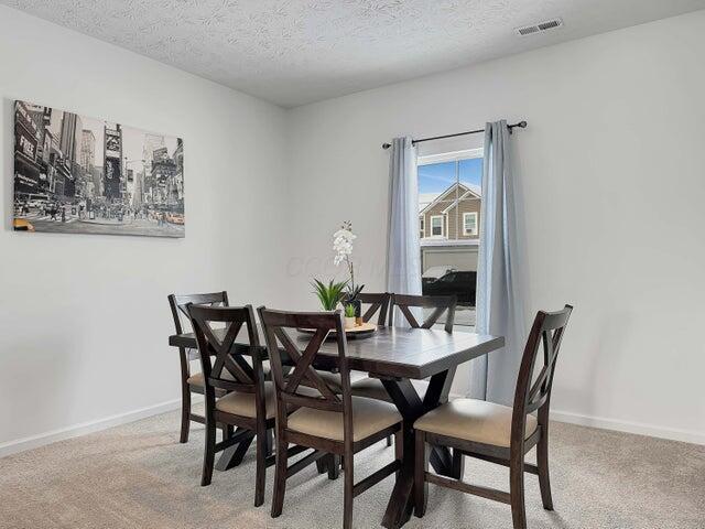 dining room with visible vents, baseboards, a textured ceiling, and light colored carpet