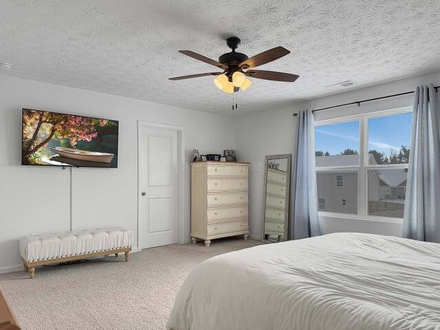 carpeted bedroom with visible vents, a ceiling fan, and a textured ceiling