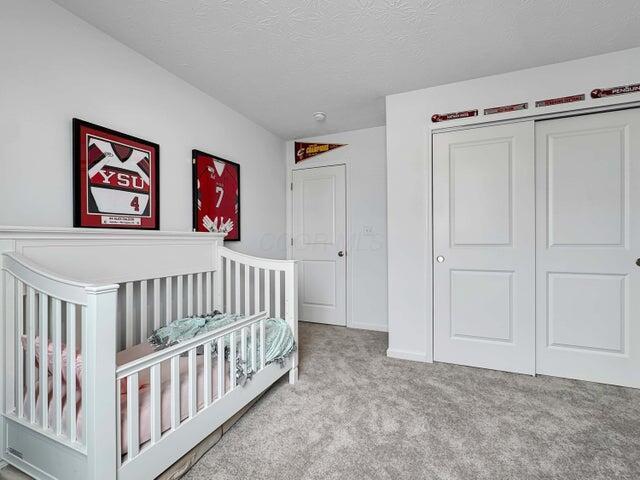 bedroom with a textured ceiling, carpet floors, a closet, and a nursery area