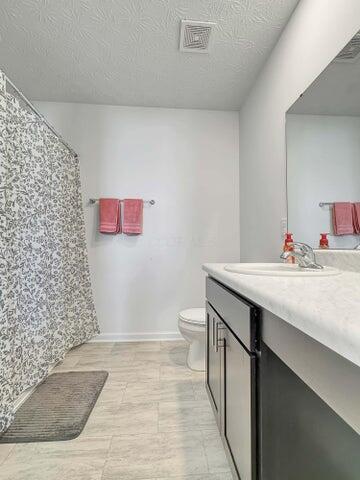 bathroom featuring a textured ceiling, toilet, a shower with shower curtain, vanity, and visible vents