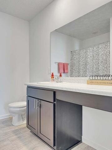 full bathroom with curtained shower, toilet, vanity, a textured ceiling, and baseboards