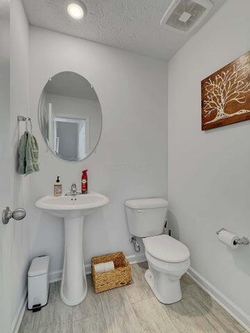 half bathroom with a textured ceiling, toilet, wood finished floors, visible vents, and baseboards